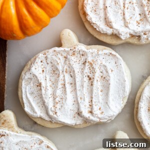 pumpkin shaped sugar cookies topped with a maple icing and sprinkled with nutmeg. a small orange pumpkin in the corner