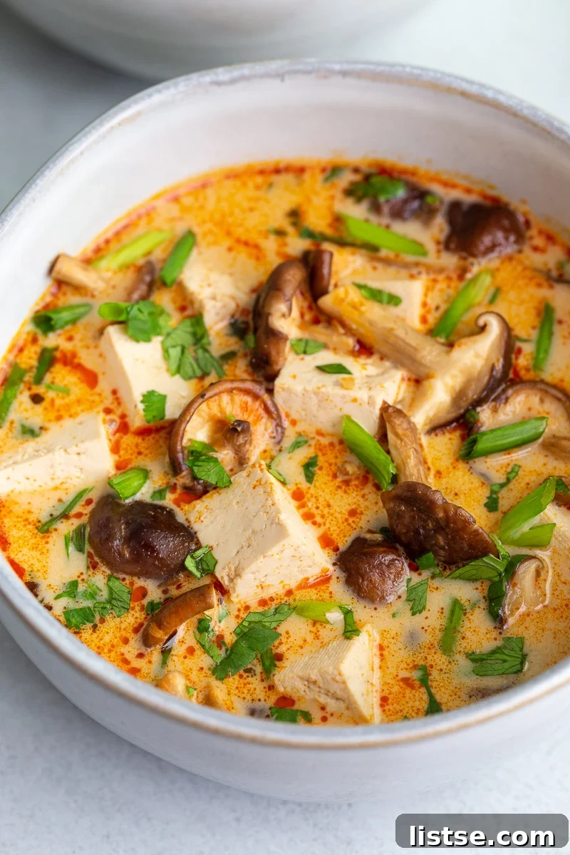 Velvety Coconut Tofu Comfort Bowl 3 A close-up of a bowl of Coconut Tofu Soup, garnished with vibrant fresh cilantro and thinly sliced green onions, ready to be enjoyed.