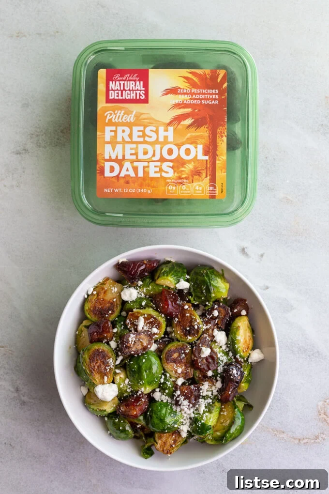 A box of Natural Delights pitted Medjool dates positioned next to a bowl brimming with cooked Brussels sprouts and chopped dates, elegantly topped with crumbled goat cheese.