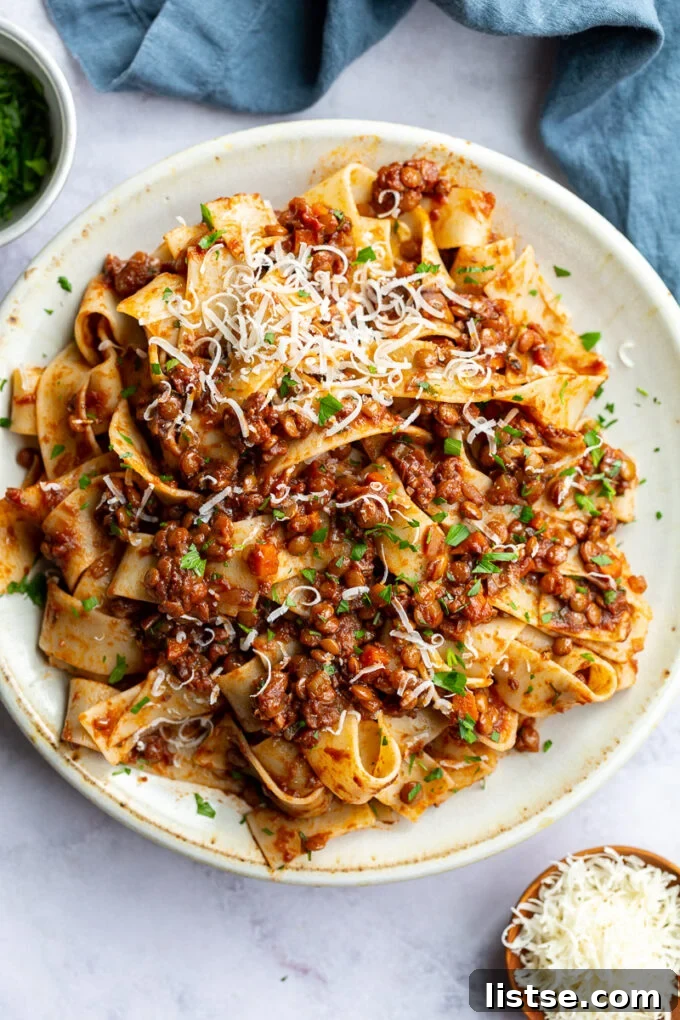 Hearty Lentil Bolognese 2 Lentil Bolognese served generously over pasta on a pristine white plate, garnished with fresh herbs.