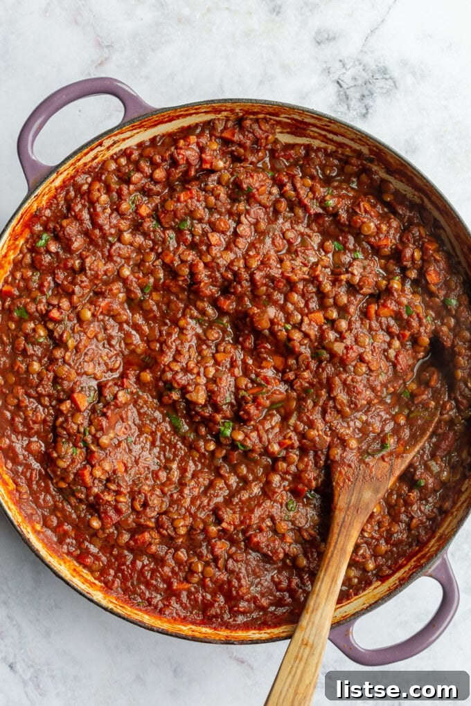 Hearty Lentil Bolognese 4 A close-up of a pot on the stove, showing various ingredients for lentil bolognese being stirred together, creating a rich pasta sauce.