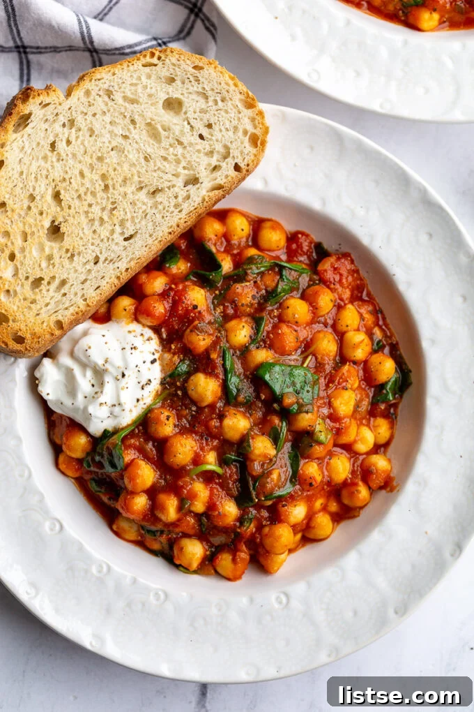 A vibrant bowl of braised chickpeas in a rich tomato sauce, generously topped with wilted spinach, ready to be enjoyed as a wholesome and satisfying meal.
