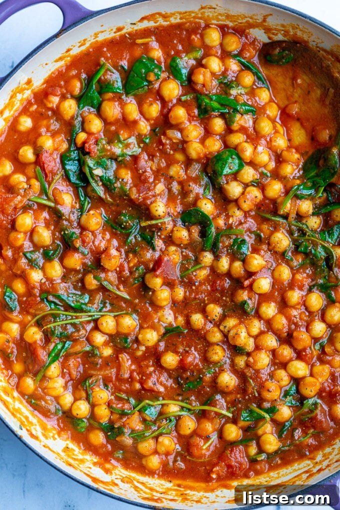 Close-up of braised chickpeas simmering in a rich red tomato sauce with wilted spinach, capturing the comforting and healthy essence of the dish.