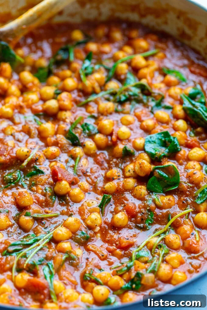 Overhead shot of a large pot filled with braised chickpeas and rich tomato sauce, being stirred, illustrating the simple cooking process.