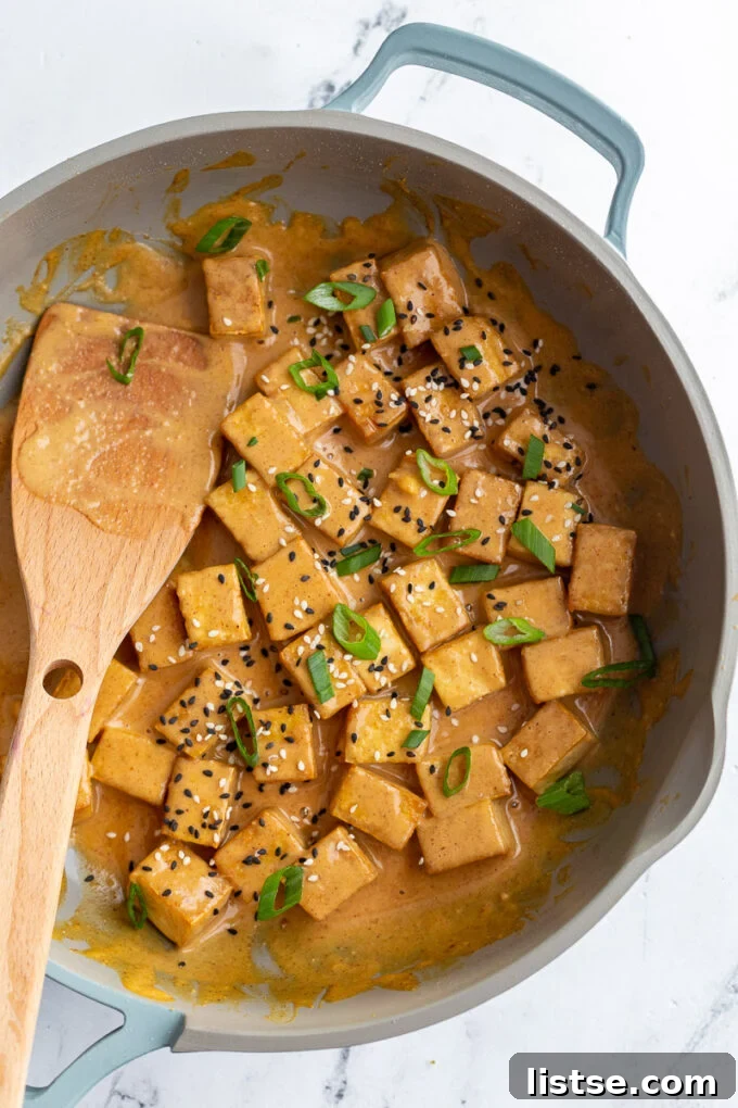 Tofu pieces being stirred in a skillet, coated in a rich peanut sauce.