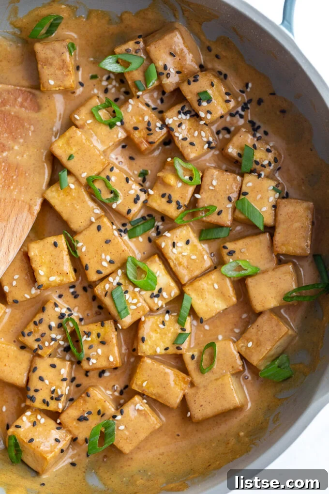 A close-up of tofu being cooked in a pan, lightly browned and ready for sauce.