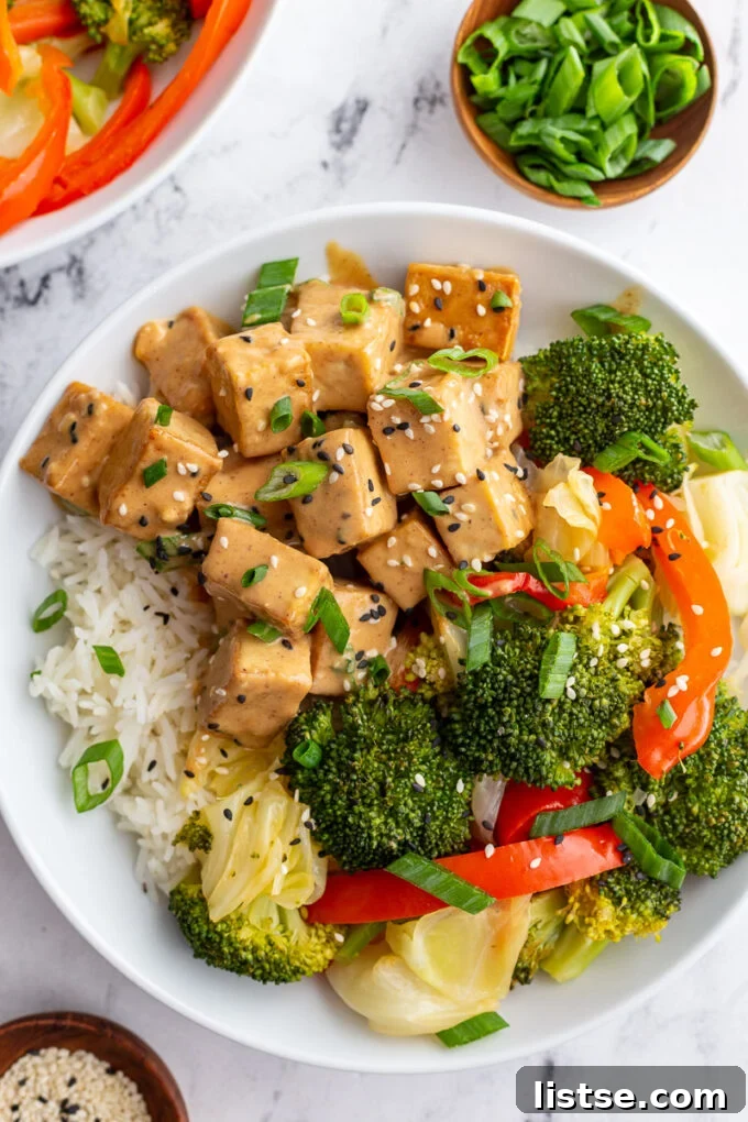 A bowl of Thai Peanut Sauce Tofu, accompanied by broccoli and bell pepper, served over rice with a final drizzle of sauce.