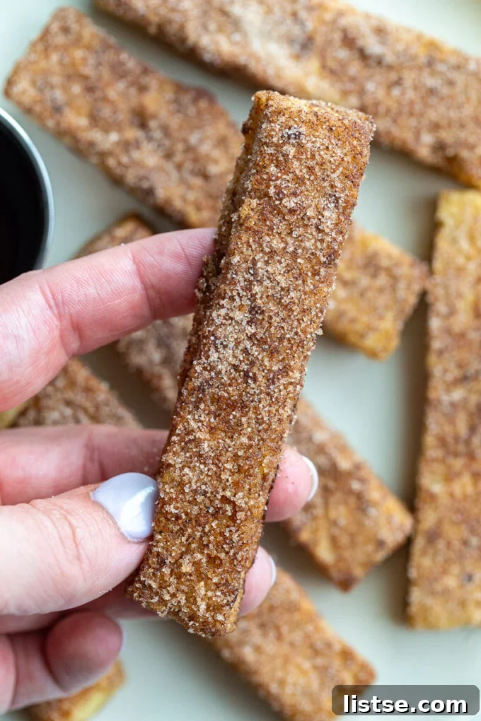 A hand holding a cinnamon sugar French toast stick, showing its crispy coating.