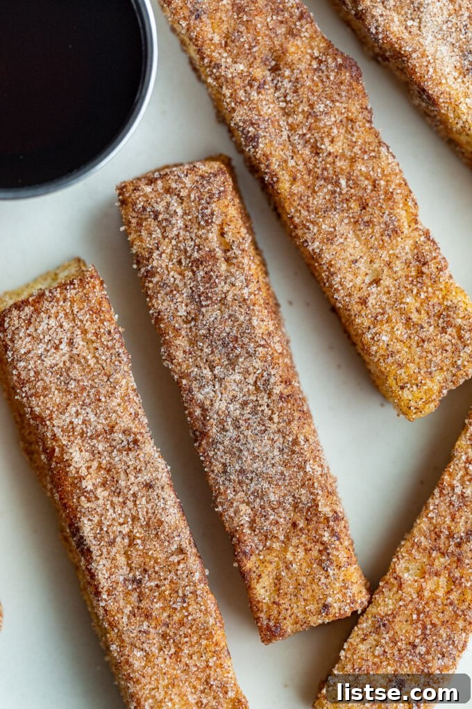 A neatly arranged plate of cinnamon sugar French toast sticks, accompanied by a small bowl of maple syrup.
