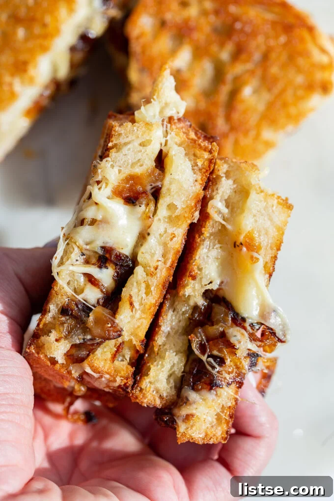Caramelized Onion grilled cheese held in a hand with cheese and onion oozing out, showing a perfect cross-section