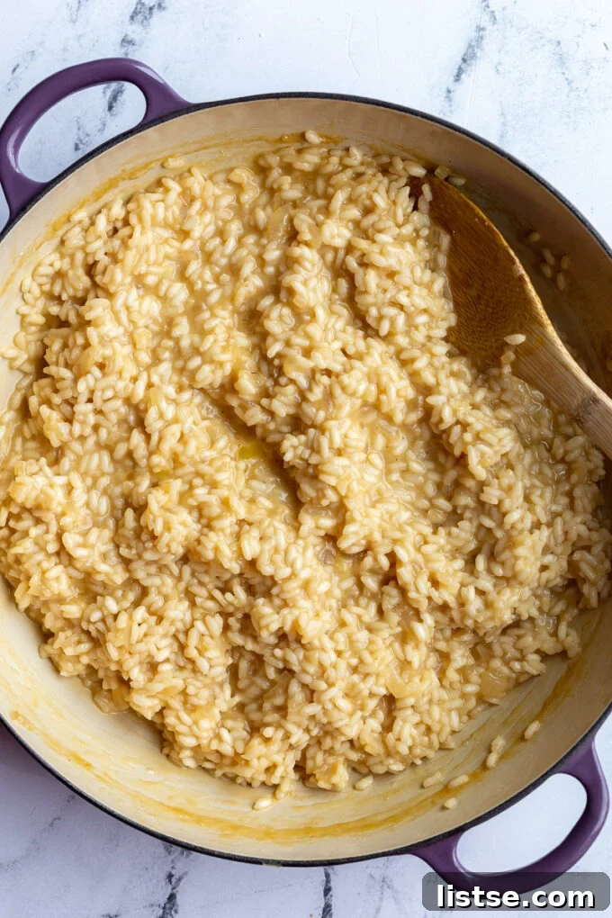 Crafting Perfect Risotto 5 A wooden spoon stirring creamy risotto in a large, wide pot on a stovetop.