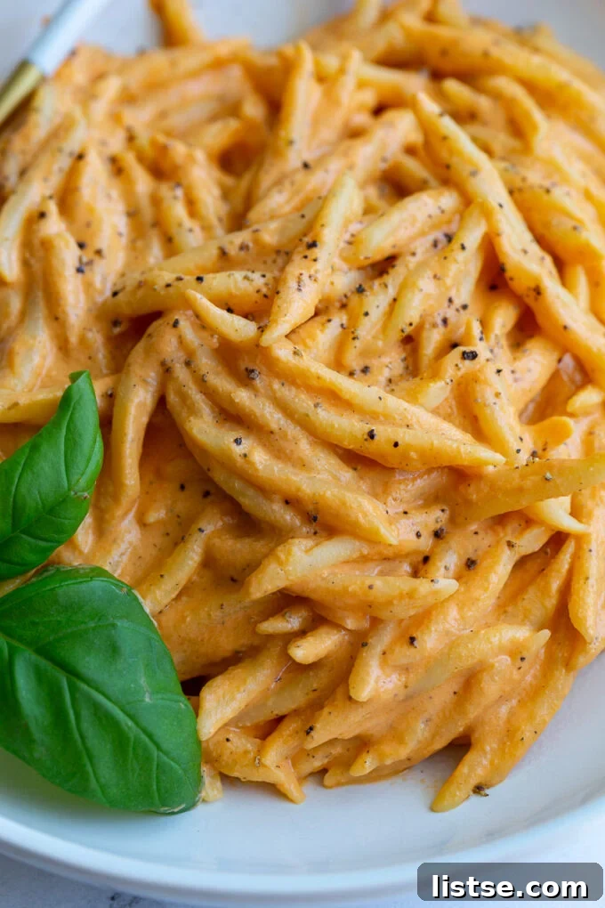 Creamy Roasted Red Pepper Tofu Pasta 5 Close-up of spiral pasta in a creamy roasted red pepper sauce, garnished with fresh basil in a wide bowl.