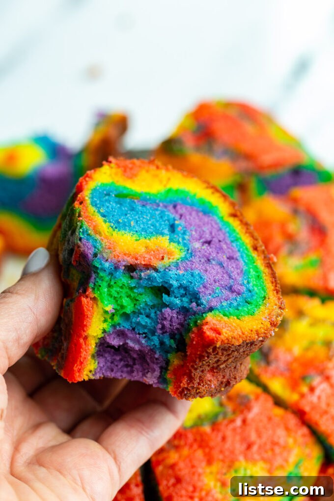 Kaleidoscope Bundt Cake 5 Hand holding a slice of colorful rainbow bundt cake.