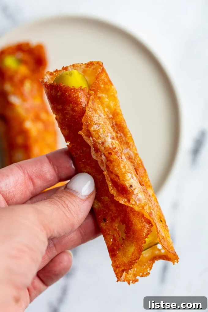 Close-up of a pickle in a blanket, showing the melted and crisped cheese around the pickle spear