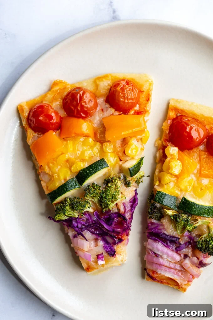 Slice of Rainbow Pizza showing off the layered vegetables and crispy crust.
