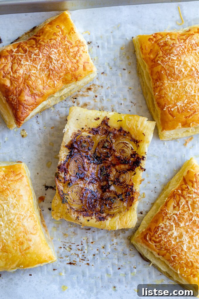 Freshly baked French Onion Tarts cooling on a baking tray lined with parchment paper, highlighting their perfectly golden puff pastry and glistening caramelized onion topping.