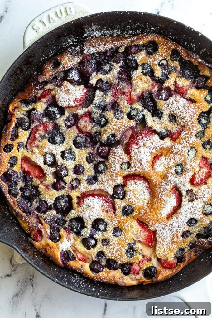 A beautifully puffed blueberry and strawberry Dutch Baby pancake in a white skillet, delicately dusted with powdered sugar, ready to be served for a delightful breakfast.