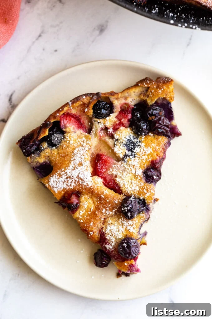 A delectable slice of blueberry and strawberry Dutch Baby pancake, generously dusted with powdered sugar, showcasing its fluffy interior and golden-brown edges.