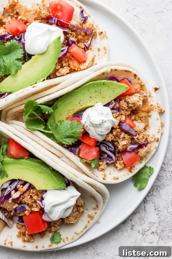 Zesty Quinoa Tofu Taco Crumbles 3 A delectable presentation of three soft tortillas, each generously loaded with the savory vegan quinoa tofu taco meat and beautifully garnished with fresh, colorful ingredients like vibrant tomatoes and verdant cilantro, arranged invitingly.