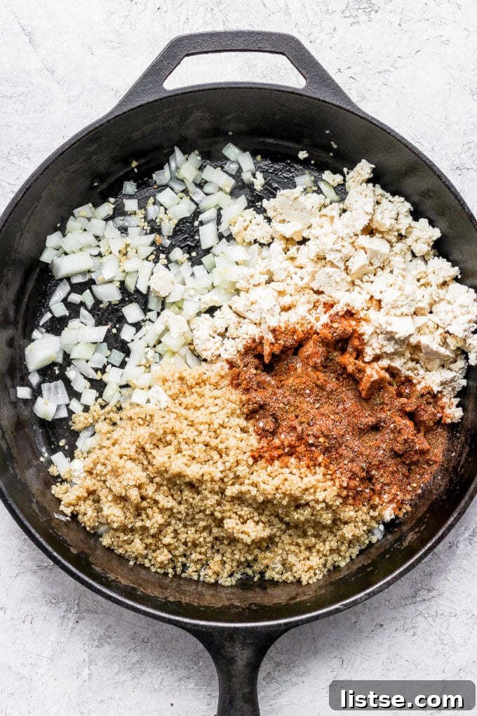 Zesty Quinoa Tofu Taco Crumbles 4 A vivid close-up of the raw ingredients in a skillet: neatly crumbled tofu, a generous sprinkle of aromatic taco seasoning, perfectly cooked quinoa, and finely chopped onion, all awaiting the cooking process.