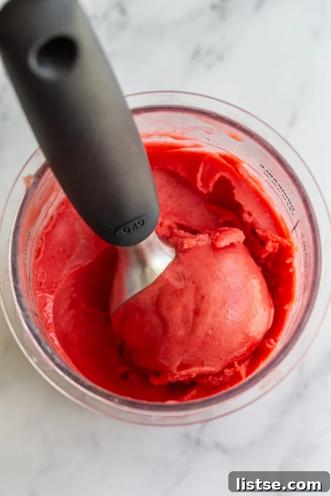 Strawberry sorbet in a Creami container with an ice cream scoop nestled inside, showcasing its creamy texture.