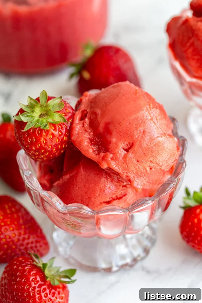 Strawberry sorbet served in an elegant ice cream dish, garnished with fresh whole strawberries around the scene.