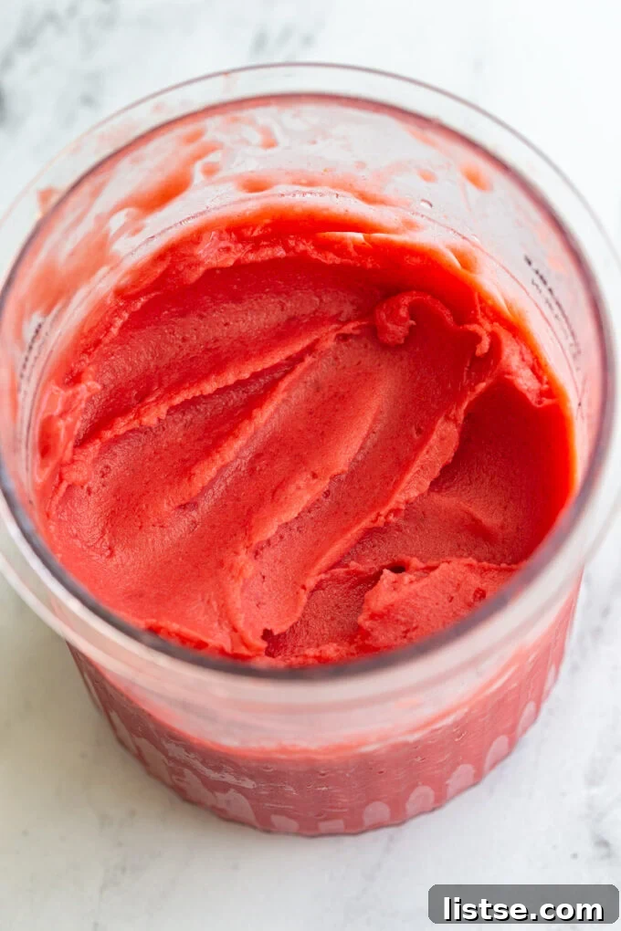 A Ninja Creami container filled with vibrant pink strawberry sorbet, topped with a spoon, highlighting its creamy texture.