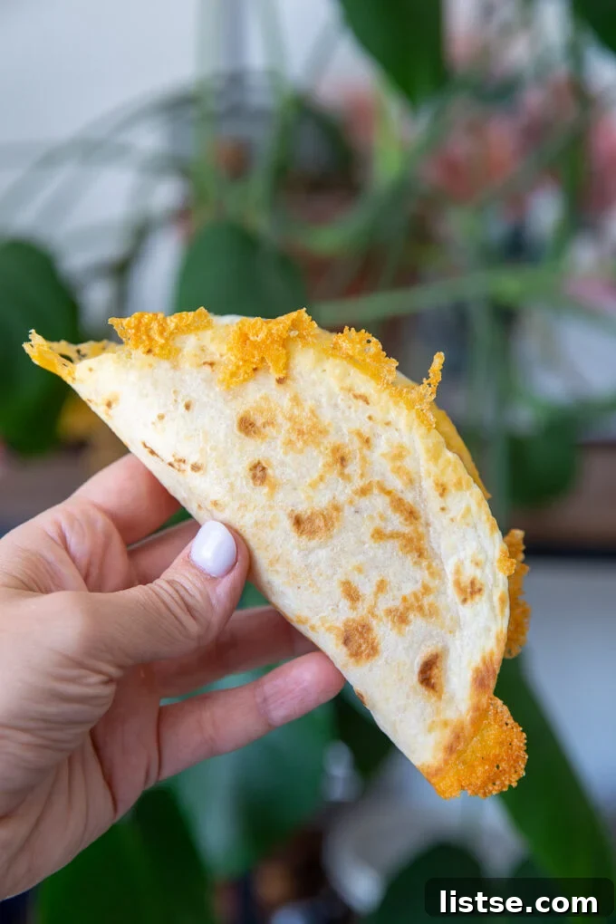 hand holding up a taco shell that's lightly browned with crispy cheese all around the edges