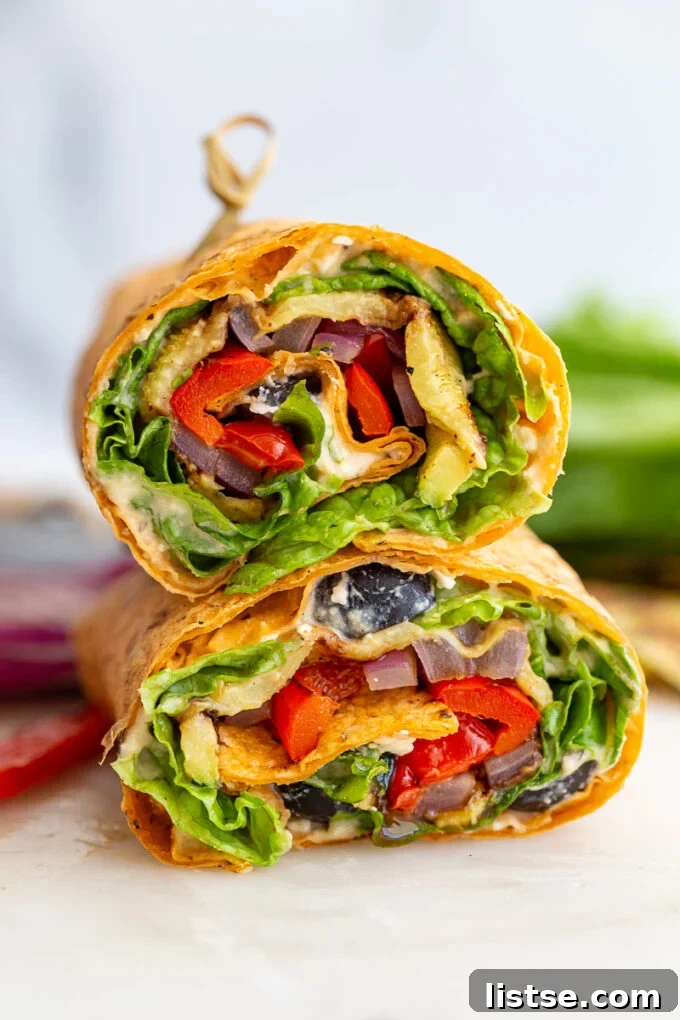 Grilled veggie wraps cut in half, revealing colorful layers of vegetables, hummus, and greens, stacked artfully.