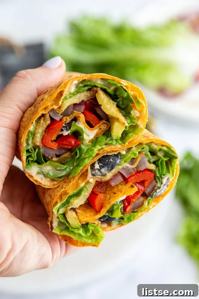 A hand holding a beautifully assembled grilled veggie wrap, cut in half to showcase the vibrant fillings.