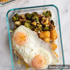 A vibrant meal prep veggie breakfast bowl featuring roasted broccoli, cauliflower, tater tots, cheese, and a fried egg.