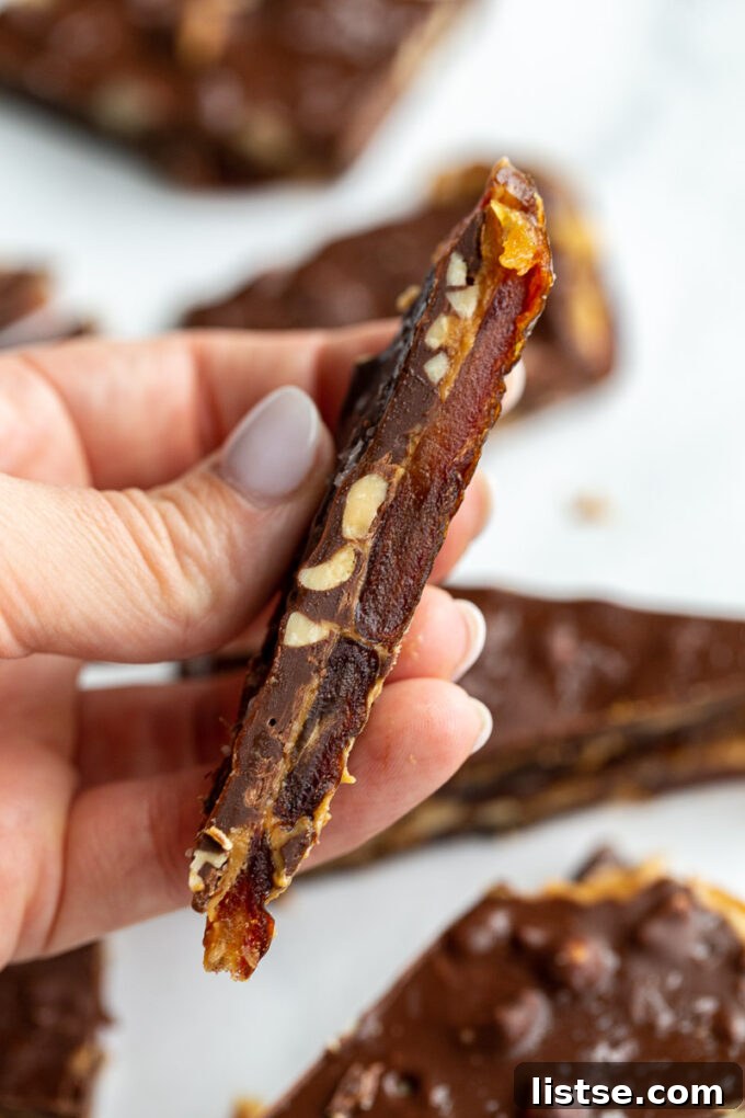 Hand holding up a piece of date bark, showcasing its delicious layers of dates, peanut butter, and chocolate with a sprinkle of sea salt.