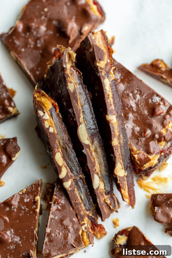 Three pieces of delicious date bark stacked sideways, showing the distinct layers of soft date base, creamy peanut butter, crunchy peanuts, and a hardened chocolate shell with sea salt flakes.