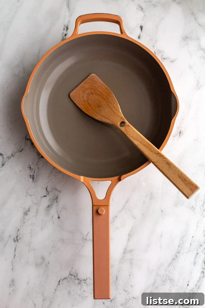 Pink Always Pan sitting on a marble board with a wooden spoon resting on the handle