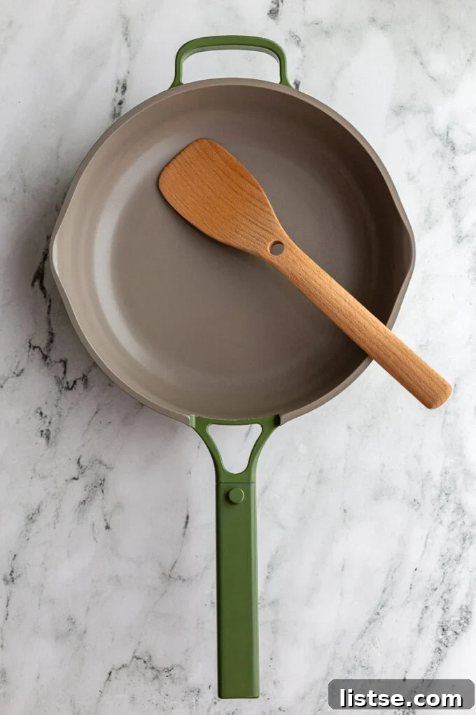Green Always Pan sitting on a marble board with a wooden spoon hanging out the side