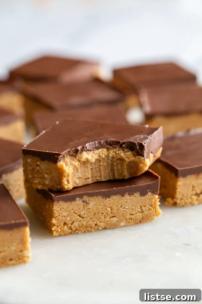 Two chocolate peanut butter bars perfectly stacked, the top one showing a clean bite revealing the rich layers, with more bars in the background.
