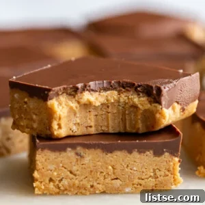 Two chocolate peanut butter bars stacked on top of each other, with one having a bite taken out, revealing the creamy filling.