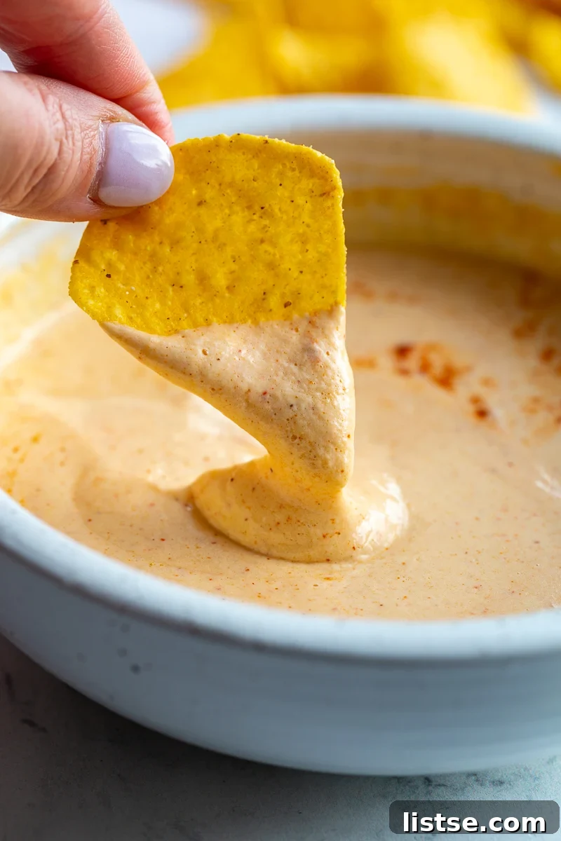 A crispy tortilla chip being dipped into a bowl of golden, creamy Cottage Cheese Queso, highlighting its appealing texture and readiness as a delicious appetizer or snack.