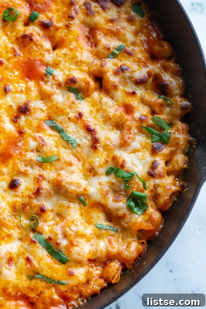 A close-up shot of the crispy, golden-brown edges of the Cheesy White Bean Tomato Bake, generously topped with fresh basil, in a white cast iron skillet.