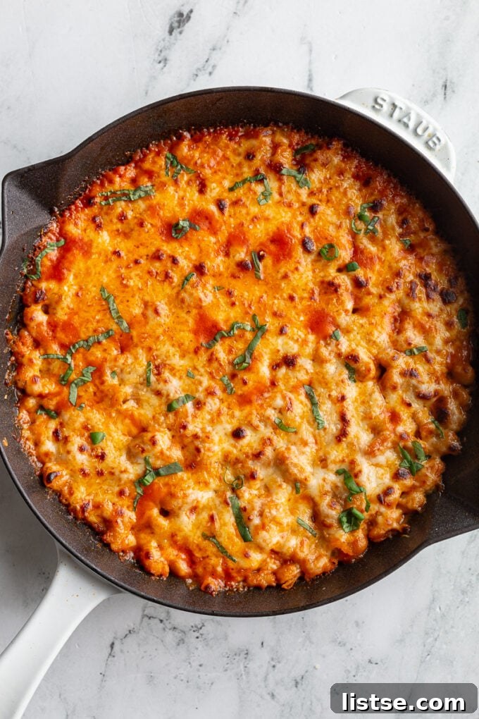 A beautifully baked Cheesy White Bean Tomato Bake in a white cast iron skillet, garnished generously with fresh basil, ready to be served.