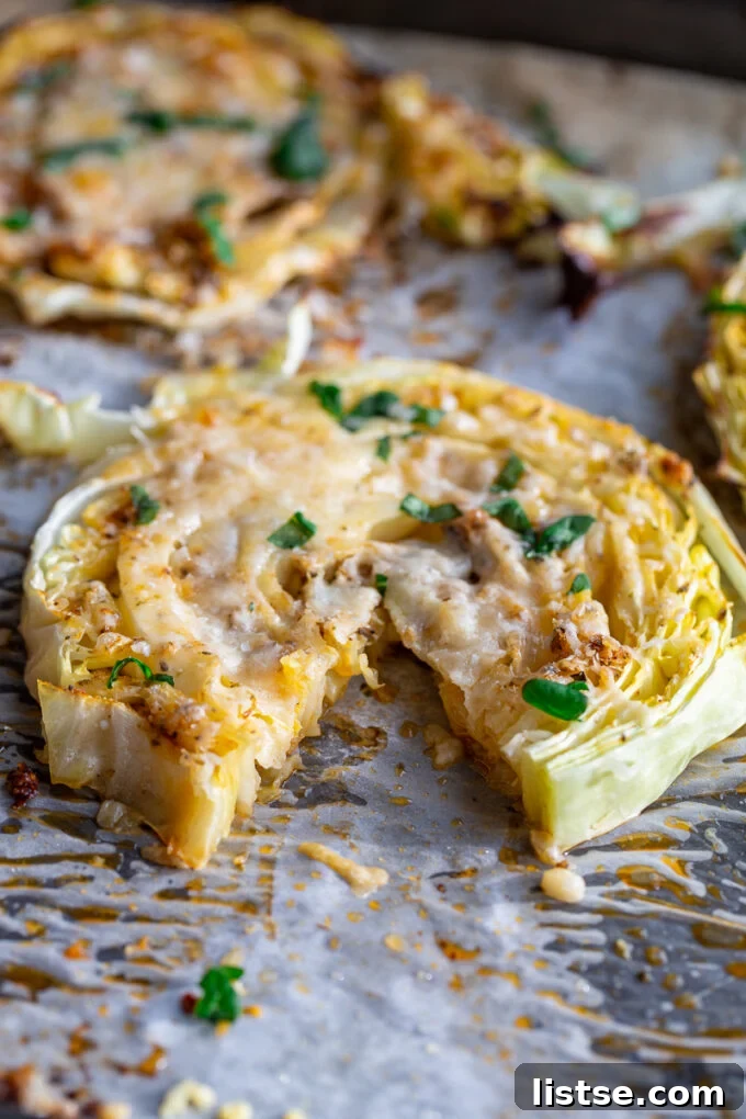 Roasted cabbage steaks covered in melted cheese and fresh basil ribbons sitting on a baking sheet. a bite has been taken out of the cabbage steak