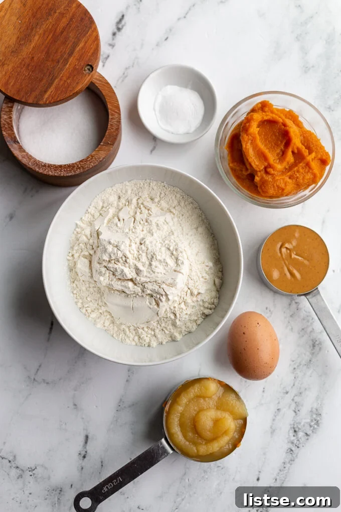 A perfect arrangement of all the wholesome ingredients needed to bake a delicious dog birthday cake: all-purpose flour, pumpkin puree, baking soda, a pinch of salt, natural peanut butter, a fresh egg, and unsweetened apple sauce.
