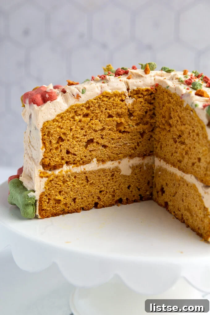 A close-up view of a slice cut from a round dog birthday cake, revealing its moist interior. The cake is covered in colorful mini dog bones, with crushed bones sprinkled on top, offering a tempting texture.