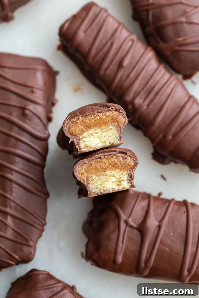 Chocolate Caramel Shortbread Bars 4 Top-down close-up of homemade Twix chocolate bars, artfully drizzled with chocolate. One bar is cut open, revealing the golden shortbread base topped with a smooth, rich caramel layer, all enrobed in chocolate.