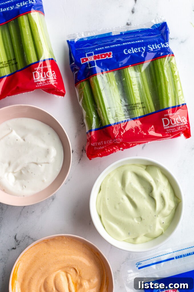 Creamy Cottage Cheese Celery Boats 3 Three bowls of whipped cottage cheese in different flavors: plain, vibrant green avocado, and zesty orange buffalo. Small bags of Dandy fresh celery are visible in the background, hinting at the perfect pairing.