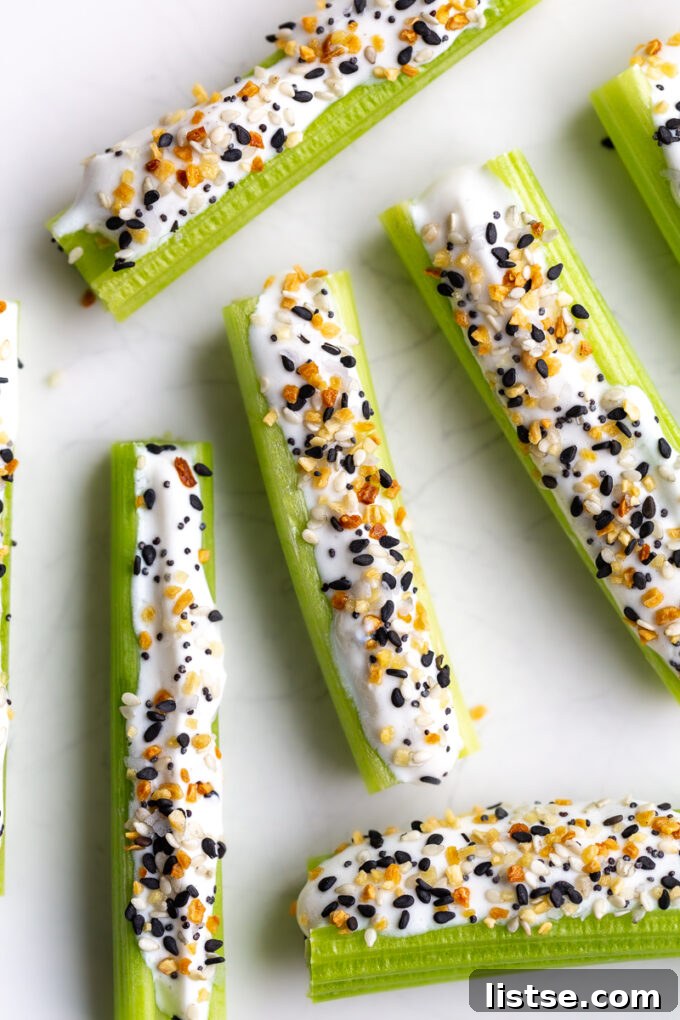 Creamy Cottage Cheese Celery Boats 5 Crisp celery sticks artfully arranged on a pristine white plate, generously topped with creamy whipped cottage cheese and a liberal sprinkle of savory Everything Bagel seasoning.