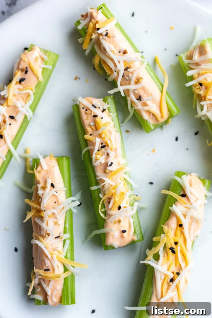 Creamy Cottage Cheese Celery Boats 7 Crisp celery sticks on a white plate generously topped with creamy buffalo whipped cottage cheese and a delightful sprinkle of shredded Mexican blend cheese.