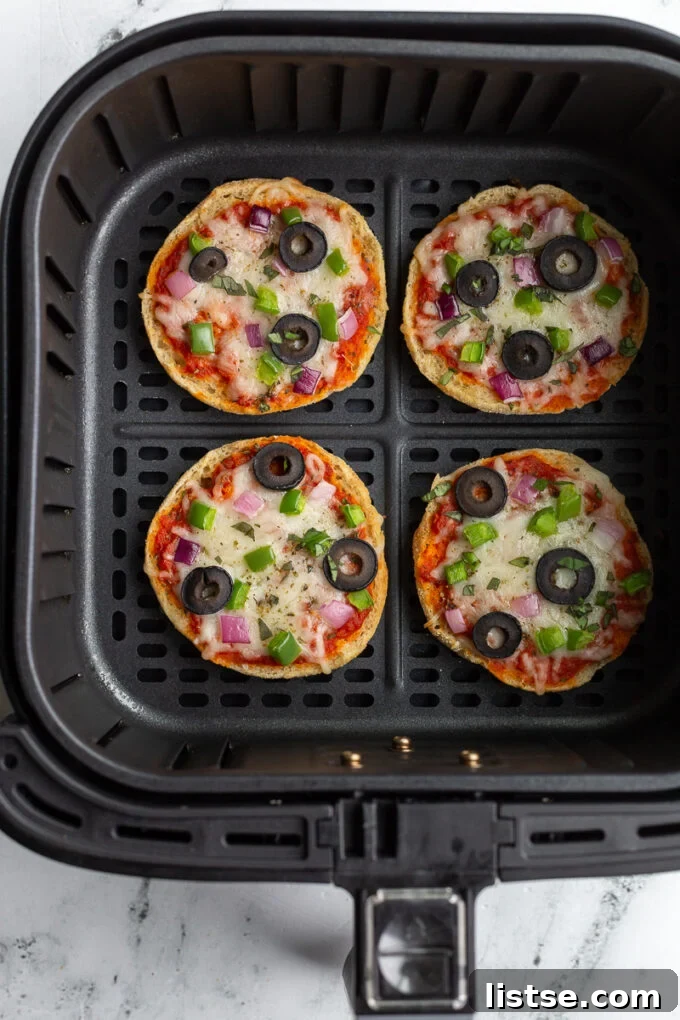 Fully cooked English Muffin veggie pizzas resting inside an air fryer basket, showing their golden crusts and melted toppings.