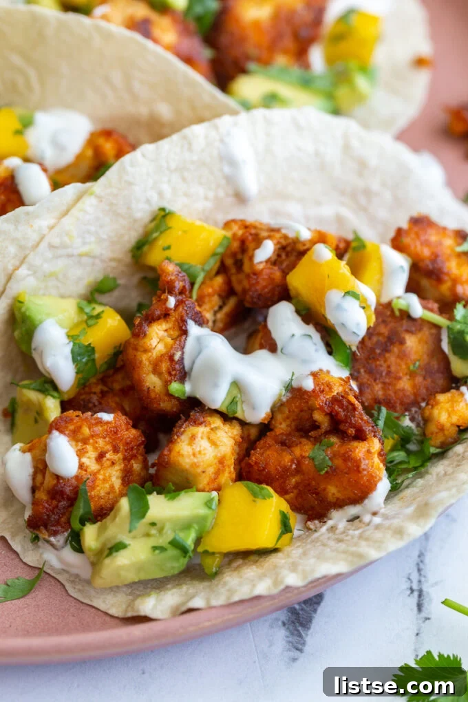 Chunks of cooked chipotle tofu in a tortilla (tacos) topped with a mango salsa and chopped cilantro. Tacos are sitting on a pink plate.