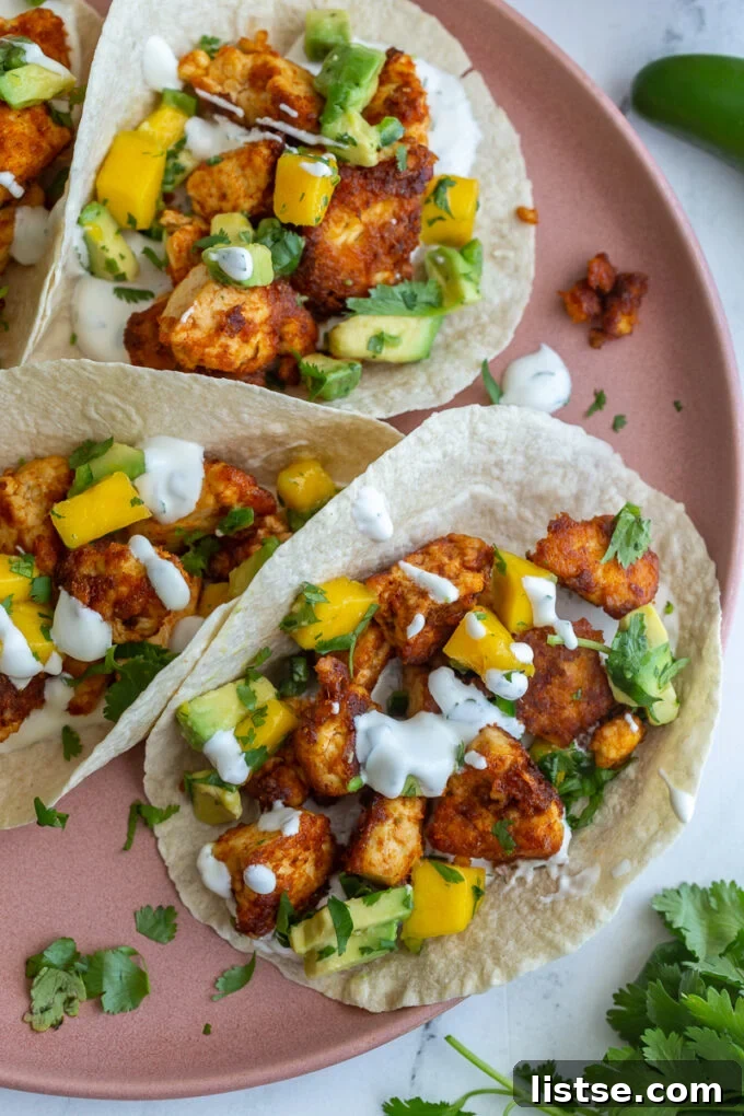 Chunks of cooked chipotle tofu in a tortilla (tacos) topped with a mango salsa and chopped cilantro. Tacos are sitting on a pink plate, ready to be enjoyed.